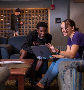 A male and female student studying at a computer in the lobby.