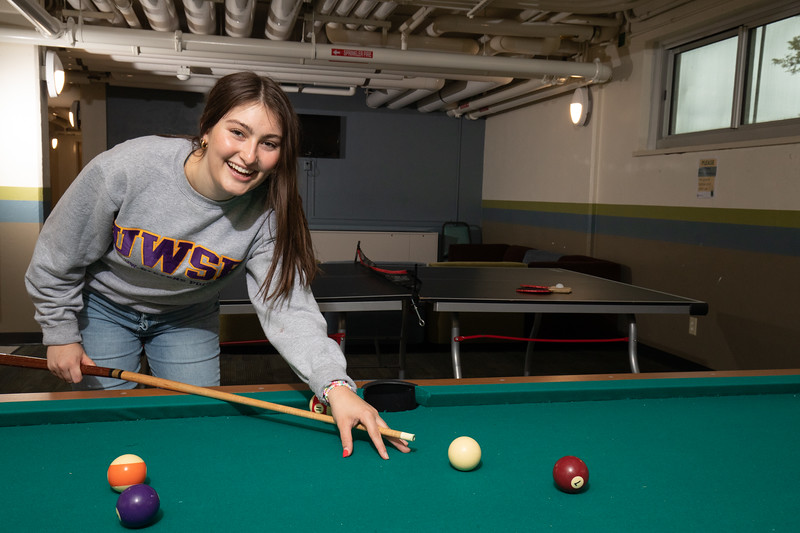 A female student playing pool in the basement.