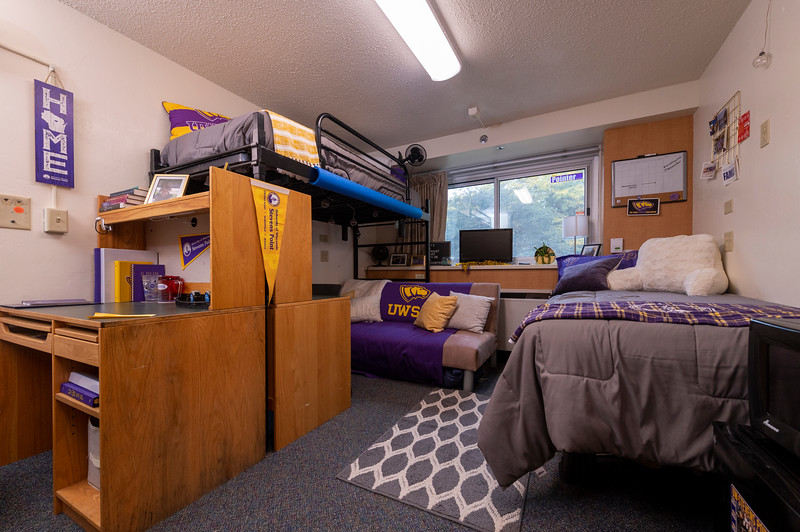 Neale Hall Tour Room featuring purple and gold bedding, posters and book materials.