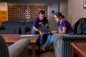 A male and female student studying at a computer in the lobby.