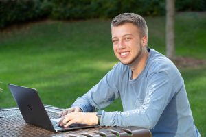 Student smiling and doing work on a laptop outside.