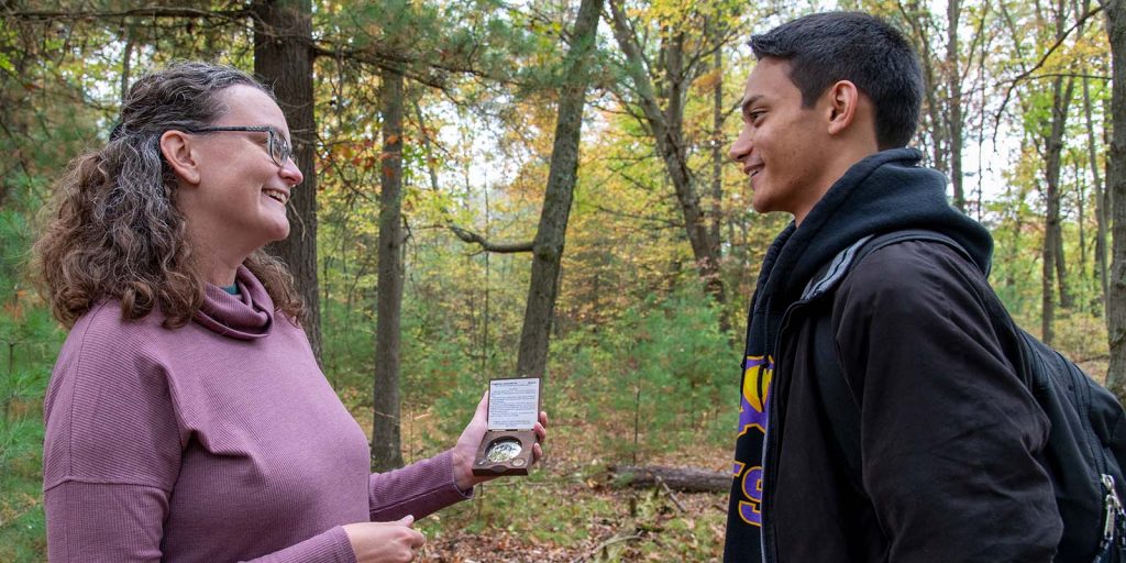 A student working with a professor in the forest.