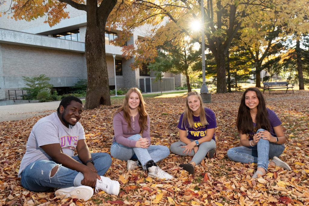 Student admissions ambassadors sitting in the fall leaves next to Albertson Hall.