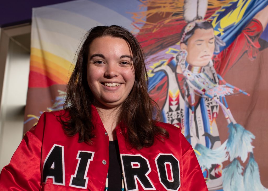 A student standing in front of a Native American mural.