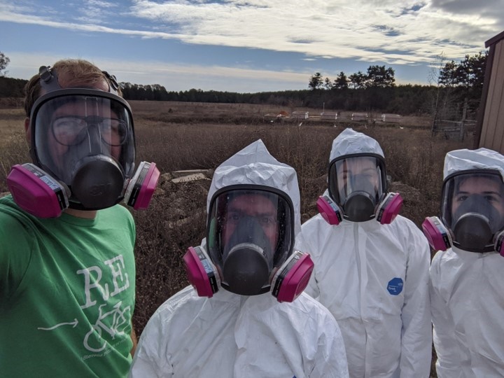 Four students in suits and gas masks doing composting research.