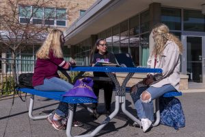 A group of students talking outside at a table on the main campus building concourse.