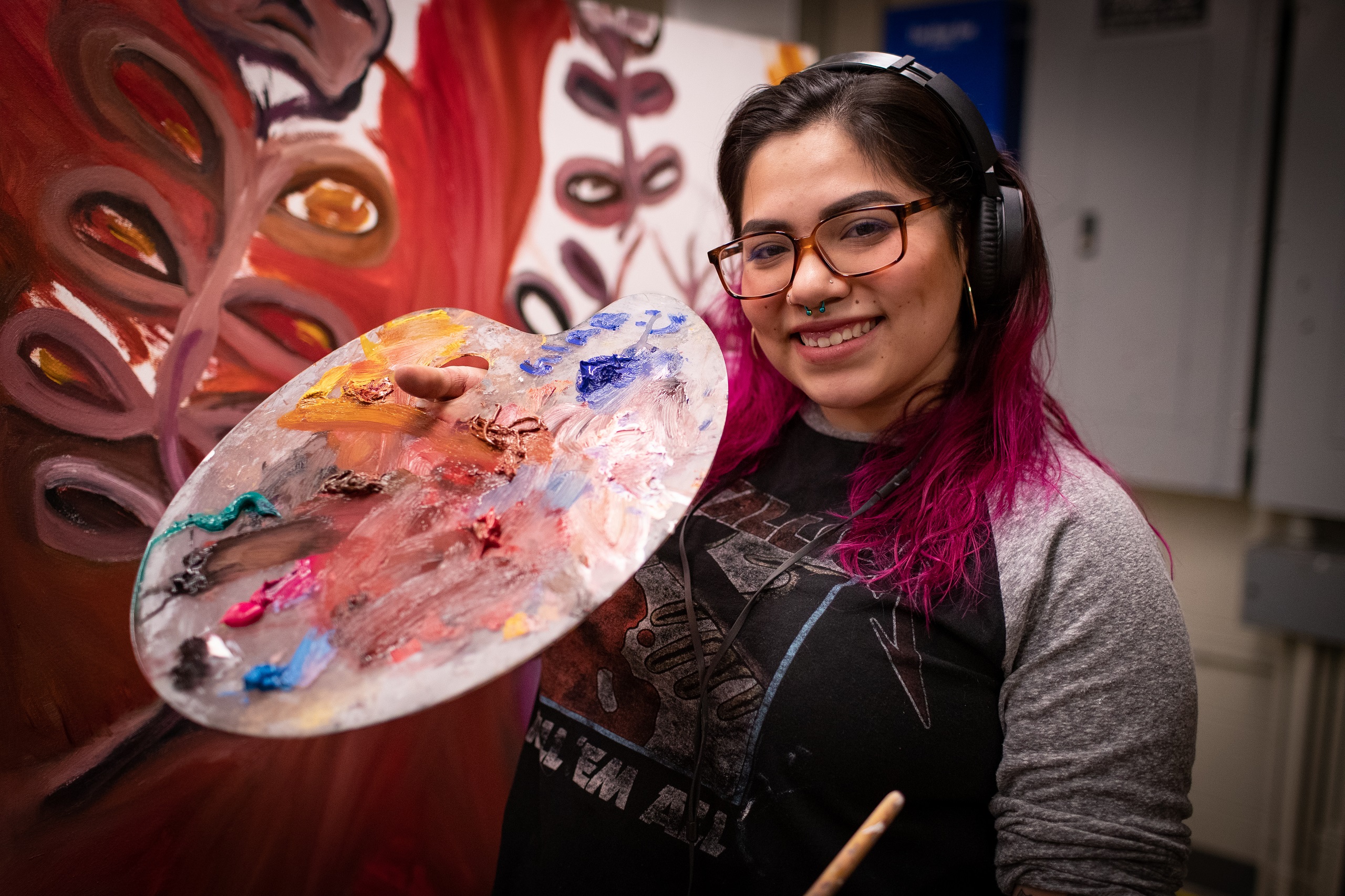 Student artist holding a paintbrush and paint while working on a project.