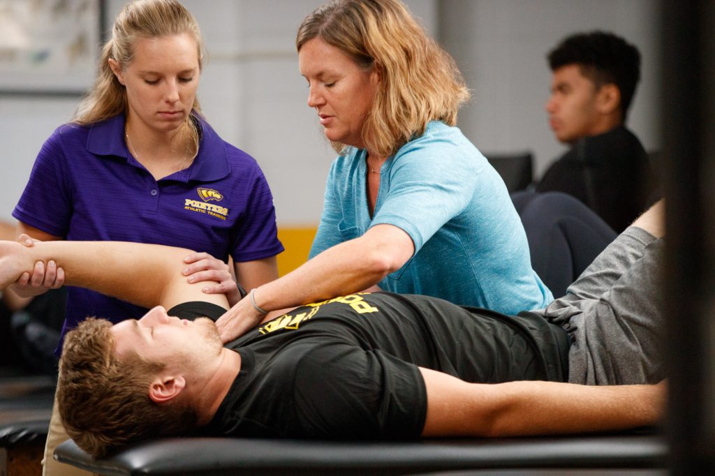 Two students and a professor working in the athletic training facility.