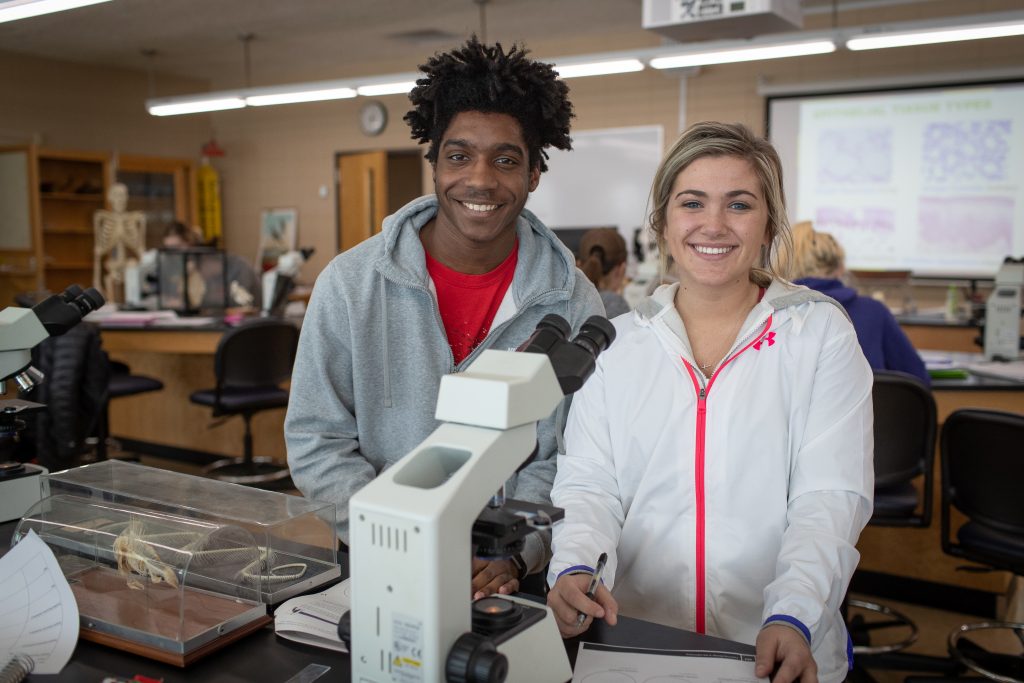 A male and female student working in science lab with a microscope.