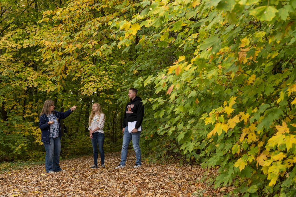 One male and one female student, along with a female professor, are walking through the arboretum pointing out different plants and features.