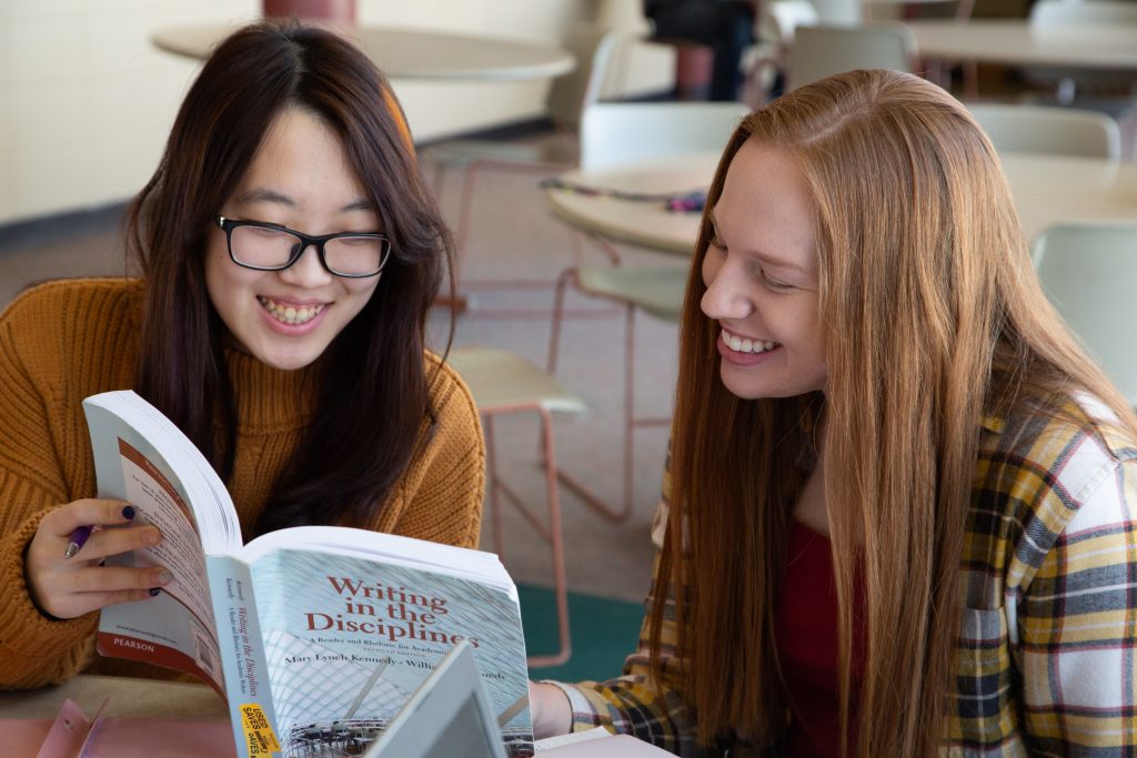 Two females smiling over a line in a book.