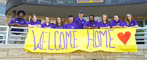 Residence life students and staff outside of hall with welcome home banner.