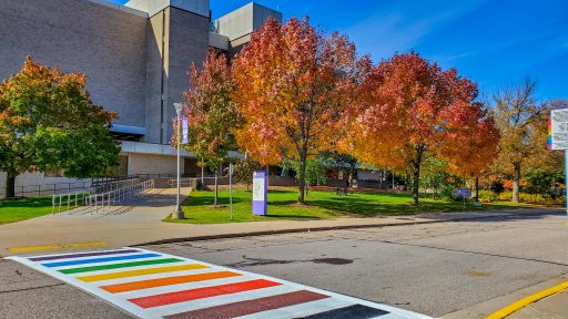 Albertson Hall fall colors on trees behind rainbow pridewalk