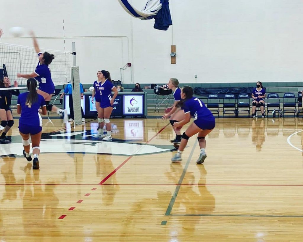 The Marshfield girls volleyball team hitting a spike during a game.