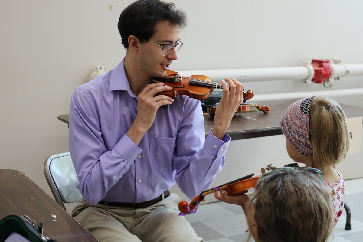 A Aber Suzuki Center teacher demonstrates a violin to several children.