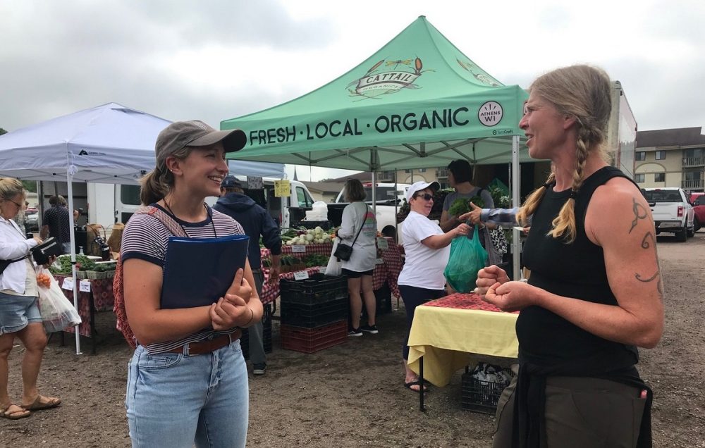 Alumna Taylor Christiansen (left), regional farmers market coordinator, is among collaborators aiming to increase access to local food and strengthen markets through community partnerships. Here, she speaks with farmer Kat Becker of Cattail Organics at the Wausau Farmer's Market.