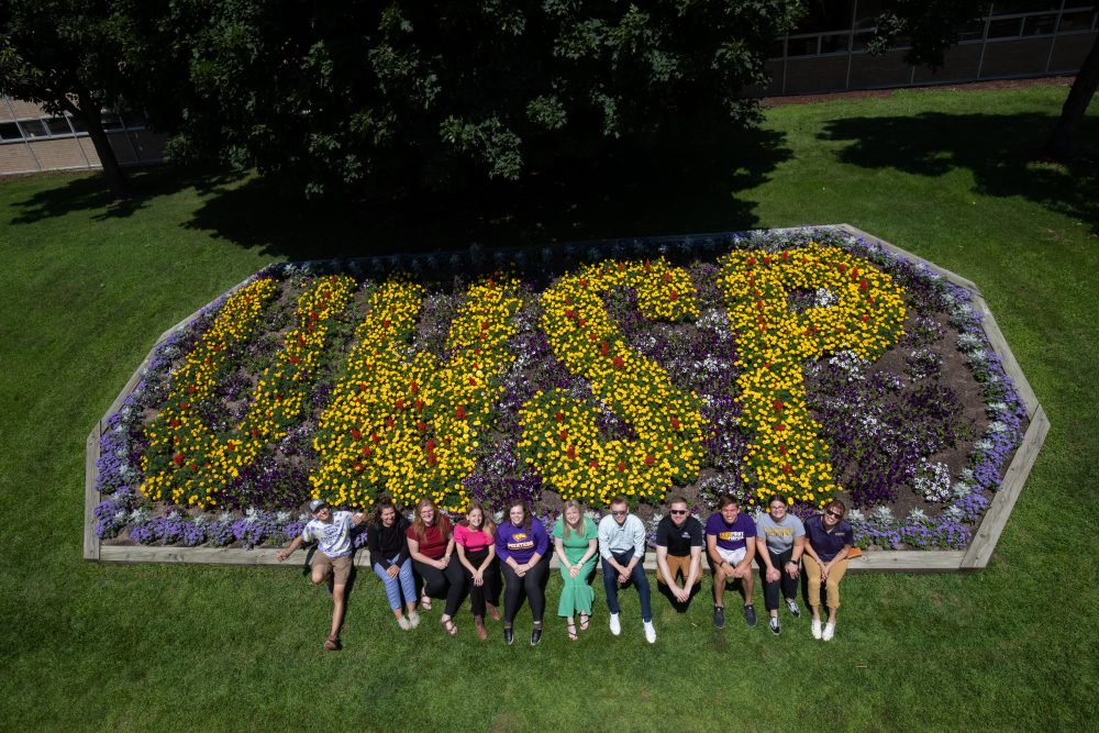 A flowerbed in the shape of U.W.S.P. with students sitting in front of it.