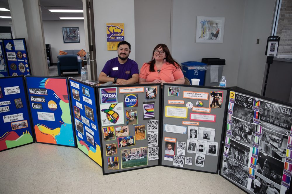 Two staff members sitting behind a large informational board.