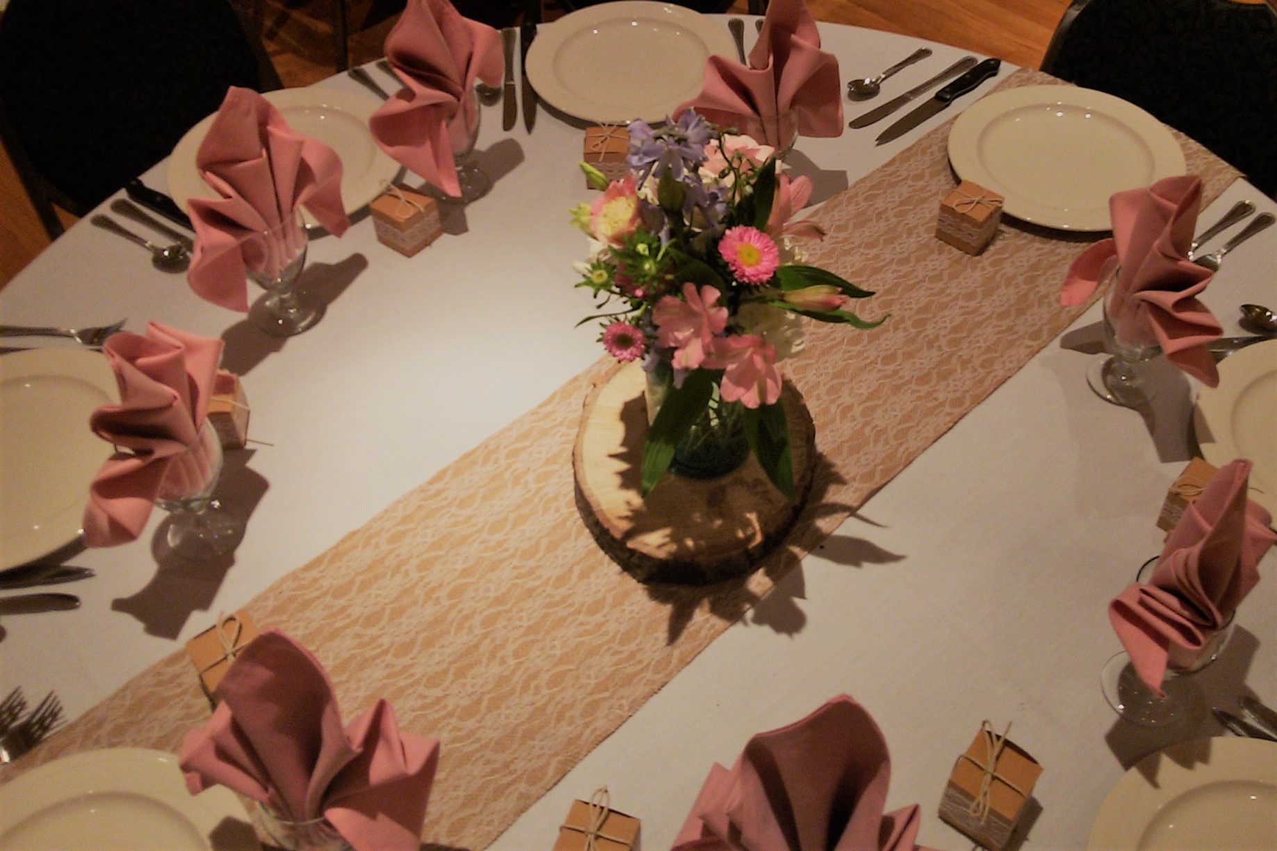 Table setting with wood plate, pink flowers and napkins, and lace runner.