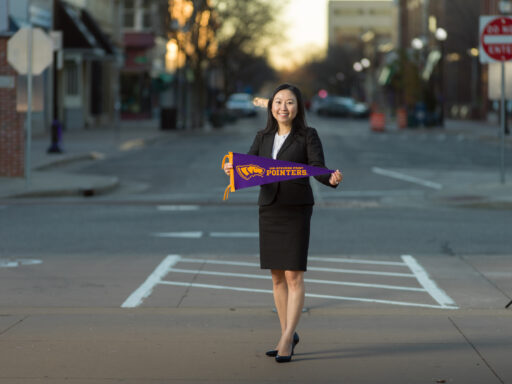 A female student in a suit holding a UWSP pennant in downtown Stevens Point