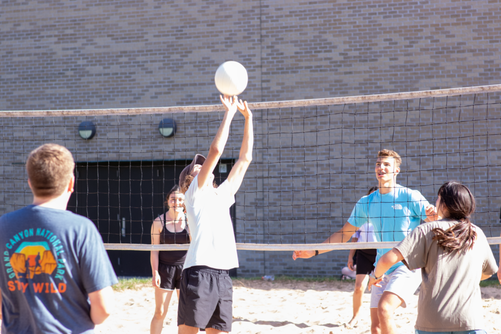 Students playing volleyball on sand volleyball court