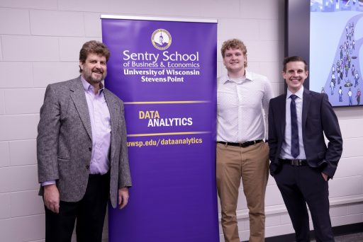 Two professors and a student standing in front of a banner that reads Sentry School of Business and Economics, Data Analytics