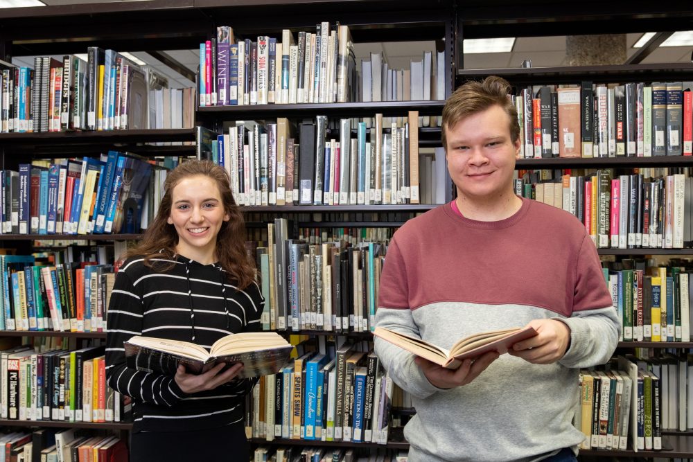Two students in a library holding books
