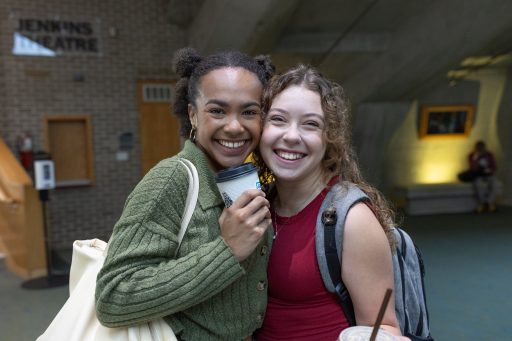 Two students standing and smiling at the camera drinking a coffee and a smoothie in the Noel Fine Arts Center.