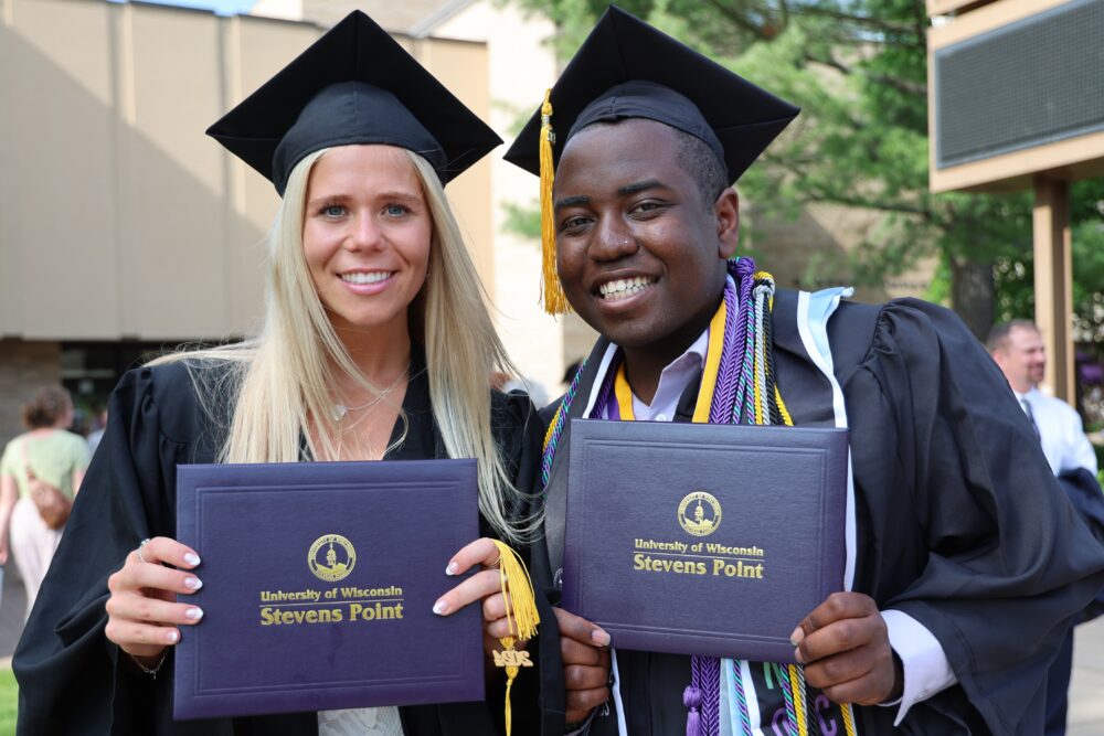 Two graduates posing with their diploma and cap and gowns